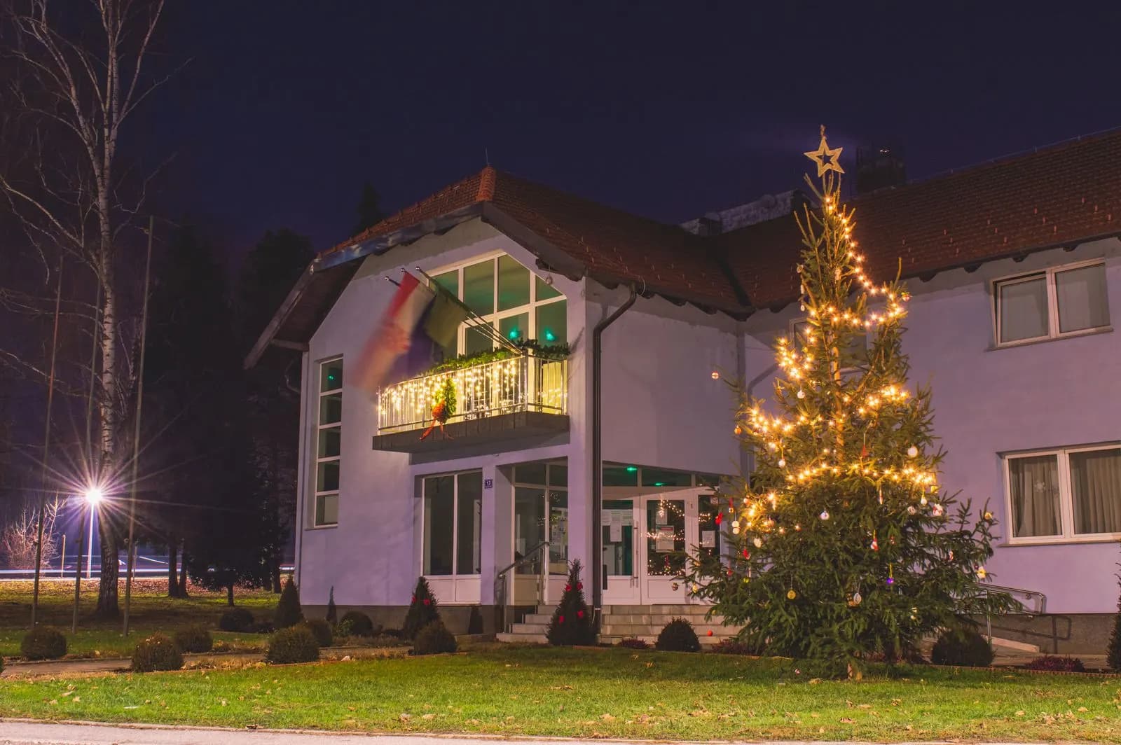 Example of a commercial building with a balcony garland and a tall evergreen wrapped in warm white lights