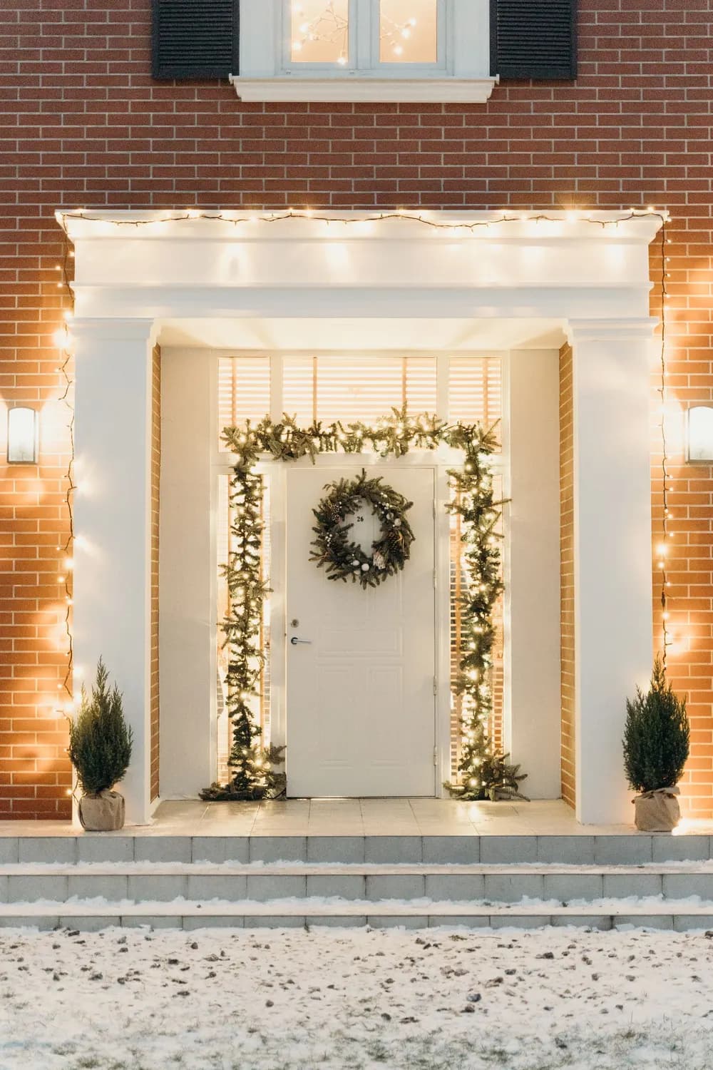 Example of a front entry outlined in warm white lights with a pre-lit garland around the door