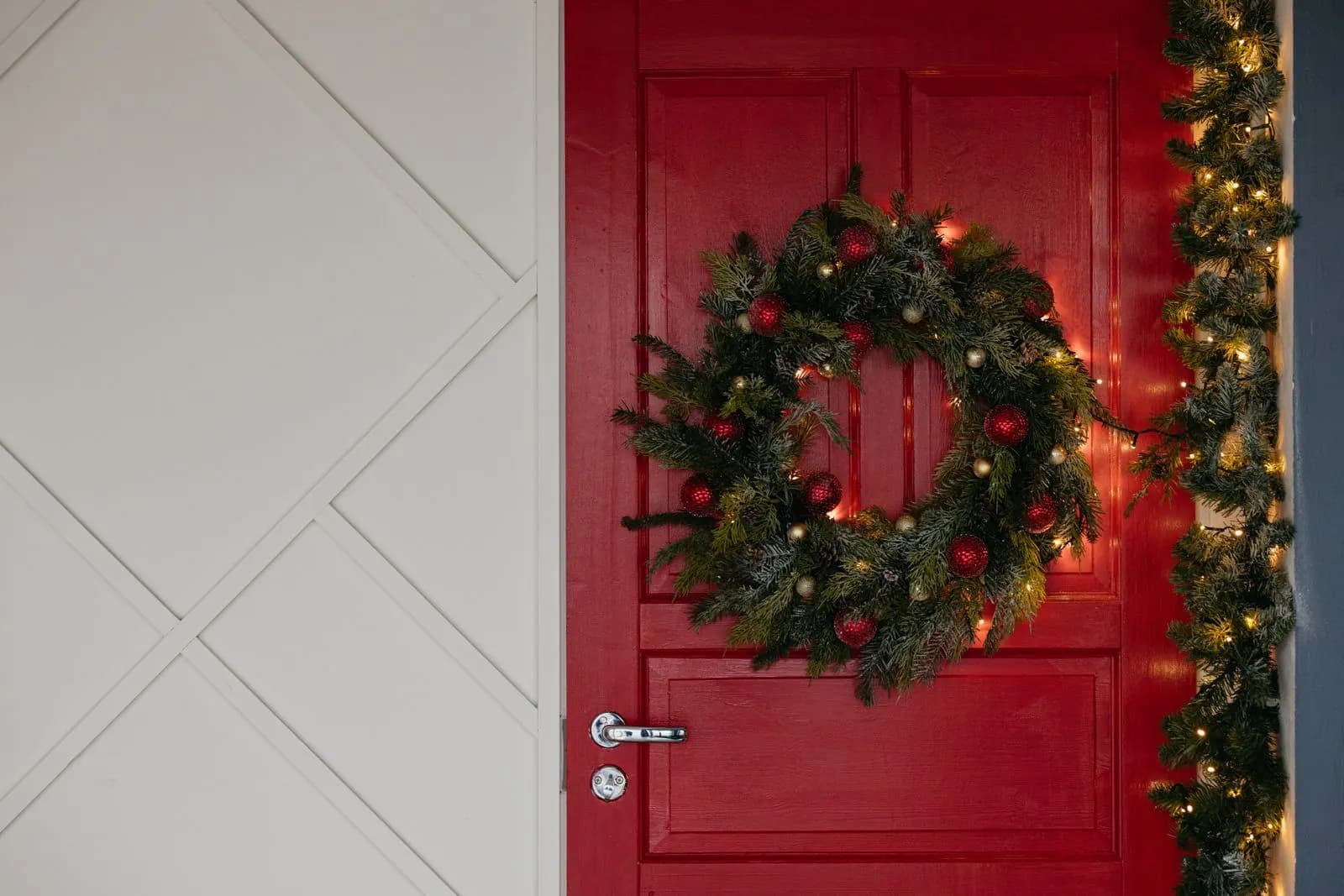 Example of a wreath on a red front door beside a garland wrapped in warm white lights