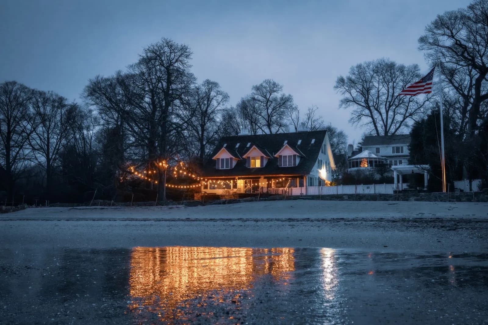 Example of warm white roofline and porch lighting on a waterfront home at dusk, reflected in the water